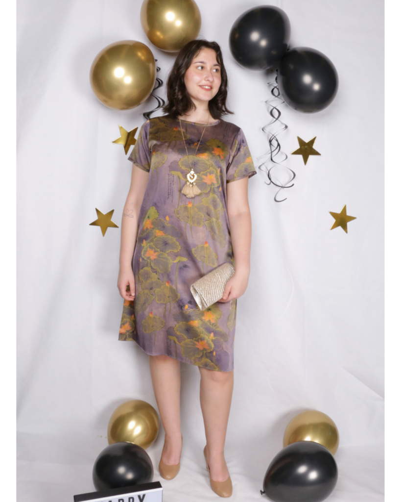 Woman in a colorful patterned dress lies on a white sheet with gold and black balloons, golden stars, and a "HAPPY NEW YEAR" lightbox, celebrating New Year’s Eve.